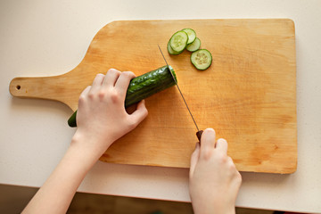 Girl cuts cucumber on a wooden board. Closeup, kitchen, hands, knife