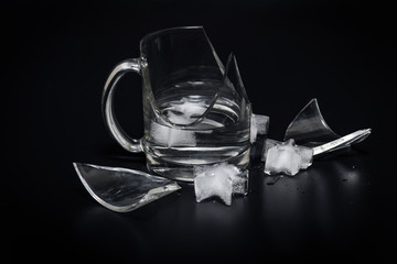 Broken glass cup with splinters, water and ice on a black background