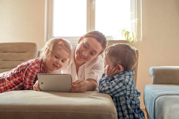 Mother with children watching cartoons on tablet and having fun at home