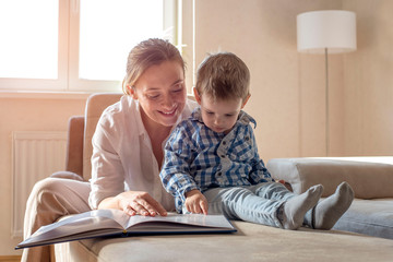 Happy mother with her little son reading book and having fun together at home