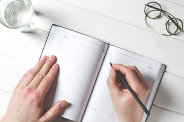 Man hands writing notes to the notebook on wooden table in home office