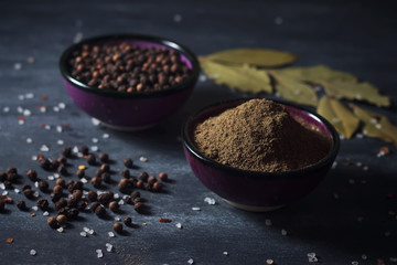 Black pepper, bay leaf and salt on a black surface