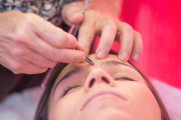 Young woman havind professional eyebrow correction at spa salon .
