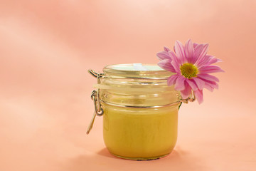 Sugar paste for depilation. Shugaring. Removing hair. Cosmetics. Honey in jar with flower on Living Coral background.