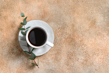 Cup of black coffee on a beige textured table with a branch of eucalyptus. Top view, copy space, minimalism style.