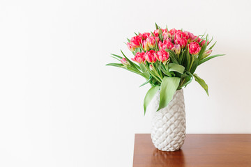 A bouquet of pink red white peony tulips in a gray modern vase on wooden tabel