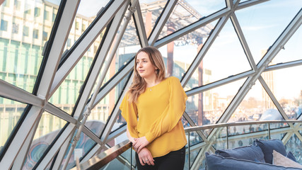 Young attractive woman in a yellow shirt looking outside in a modern glass building