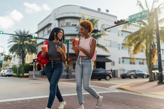 USA, Florida, Miami Beach, two happy female friends having a soft drink crossing the street