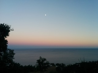 Fototapeta premium Gradient sunset over the Black Sea, Crimea, Russia. Pink, yellow, purple-blue horizon. There is a big moon in the sky