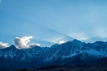 Fototapeta na wymiar blue sky, clouds, slanted beams of sunlight over peaks of Eastern Sierra Nevada, California, USA