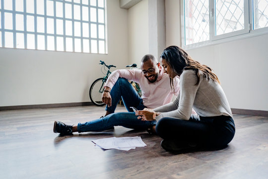 Smiling businessman and businesswoman sitting on the floor with cell phone and documents