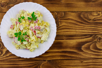 Salad with crab sticks, sweet corn, chinese cabbage, eggs and mayonnaise on wooden table