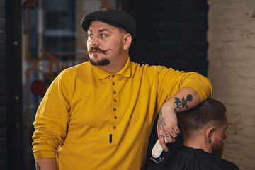Barber making haircut of attractive bearded man in barbershop