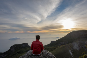 A man sitting and enjoying sunrise on the rock at the top of Gede Pangrango Mountain