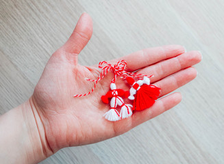 Bulgarian traditional spring decor martenitsa, holding in hand, wooden background. Baba Marta holiday, backdrop.