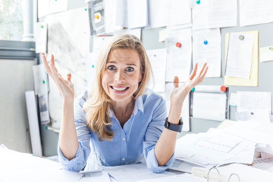Portrait of stressed woman sitting at desk in office surrounded by paperwork