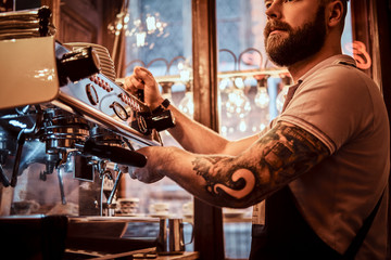 Handsome tattooed barista with stylish beard and hairstyle working on a coffee machine in a coffee shop or restaurant - Powered by Adobe