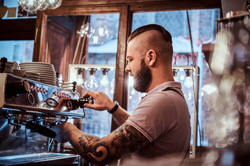 Handsome tattooed barista with stylish beard and hairstyle working on a coffee machine in a coffee shop or restaurant