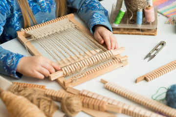 A little girl learns process to thick threads. Creating a picture by weaving.