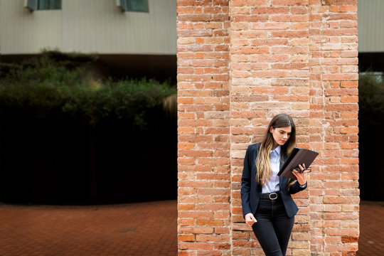 Young businesswoman standing at brick column using tablet