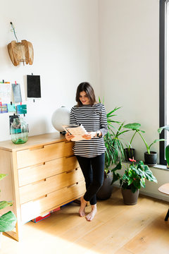 Young woman standing at commode at home reading a booklet