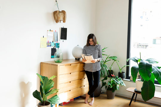 Young woman standing at commode at home reading a booklet