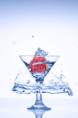 Glass with water and ice. Beautiful frozen nuclear explosion of freshness with splashes of water, in a cocktail glass with strawberries, on a white background.