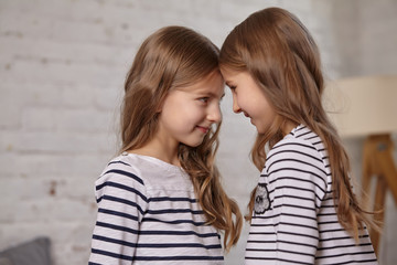 The image of two little sisters sitting on the bed in the room.
