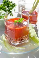 Drink red tomato juice. Tomato juice is poured into a transparent glass with parsley and herring, on a white background, illuminated by sunlight.