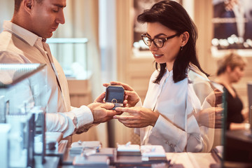 Elegantly dressed male and his girlfriend choose wedding rings in a luxury jewelry store