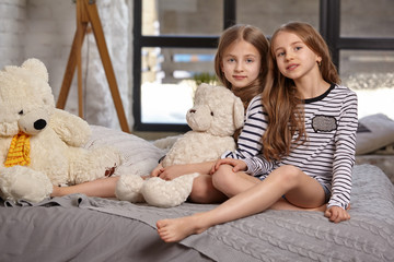 The image of two little sisters sitting on the bed in the room.