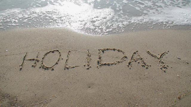 "Holiday" verb written on the sand. Wave washes away the inscription holiday.
