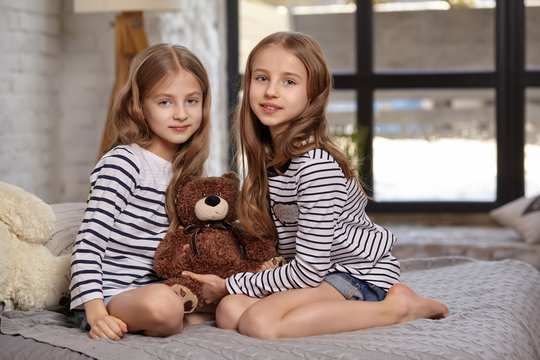 The image of two little sisters sitting on the bed in the room.