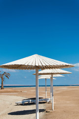 White parasols and sun loungers on the sandy beach by the sea.