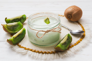 Yogurt with kiwi slices on a wooden white background.