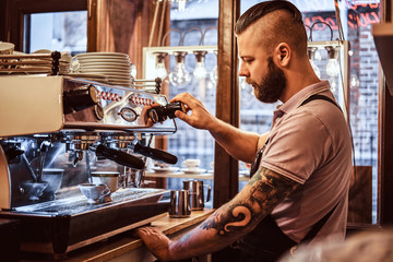 Handsome barista in uniform preparing a cup of coffee for a customer in the coffee shop