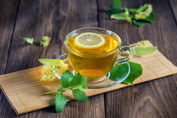 Tea with lemon, mint and lime blossom. Cup with fragrant lime tea, standing on a wooden table, in the rays of sunlight.