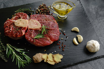 Raw Osso Buco steak on a black stone surrounded by spices