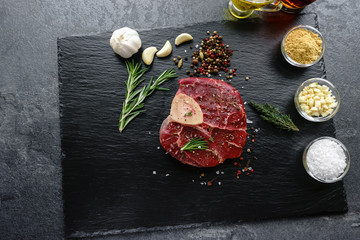 Raw Osso Buco steak on a black stone surrounded by spices