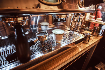 Close-up photo of a portafilter and cup with cappuccino next to a coffee machine in the restaurant of a coffee shop