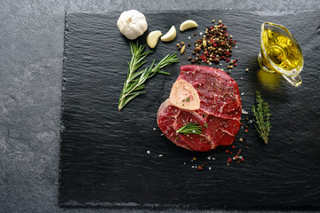 Raw Osso Buco steak on a black stone surrounded by spices