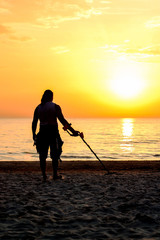 Man silhouette with metal detector on the beach