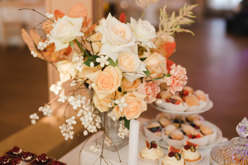 Coziness and style. Modern event design. Table setting at wedding reception. Floral compositions with beautiful flowers and greenery, candles, laying and plates on decorated table.