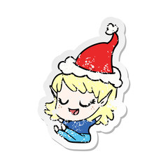 happy distressed sticker cartoon of a elf girl sitting wearing santa hat