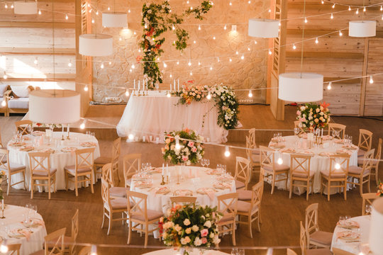 Coziness and style. Modern event design. Table setting at wedding reception. Floral compositions with beautiful flowers and greenery, candles, laying and plates on decorated table.