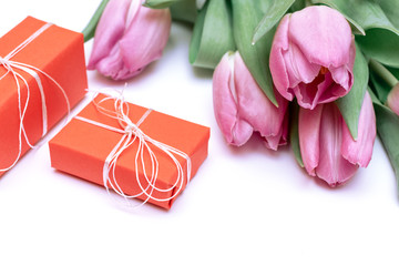A bouquet of pink spring flowers tulips and red gift boxes jn white background