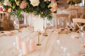 Coziness and style. Modern event design. Table setting at wedding reception. Floral compositions with beautiful flowers and greenery, candles, laying and plates on decorated table.