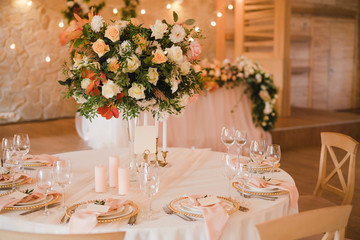 Coziness and style. Modern event design. Table setting at wedding reception. Floral compositions with beautiful flowers and greenery, candles, laying and plates on decorated table.