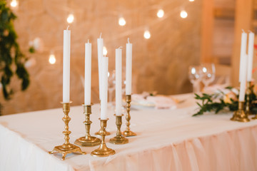 Coziness and style. Modern event design. Table setting at wedding reception. Floral compositions with beautiful flowers and greenery, candles, laying and plates on decorated table.