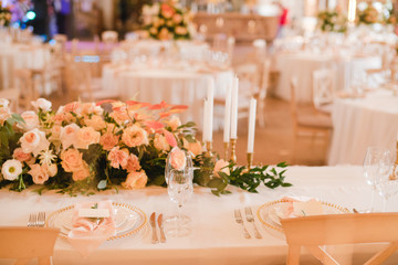 Coziness and style. Modern event design. Table setting at wedding reception. Floral compositions with beautiful flowers and greenery, candles, laying and plates on decorated table.